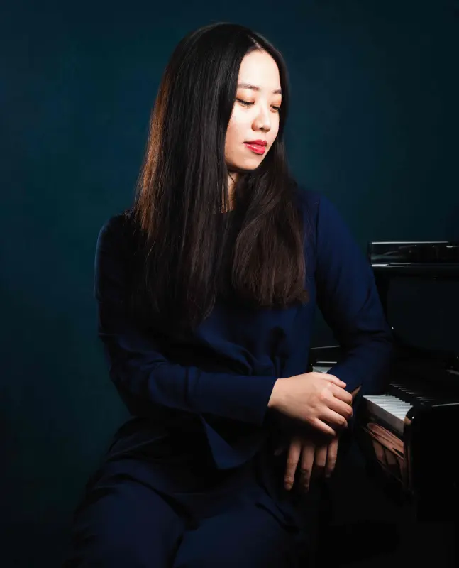 Tsuzumi Namikawa zit naast een piano.